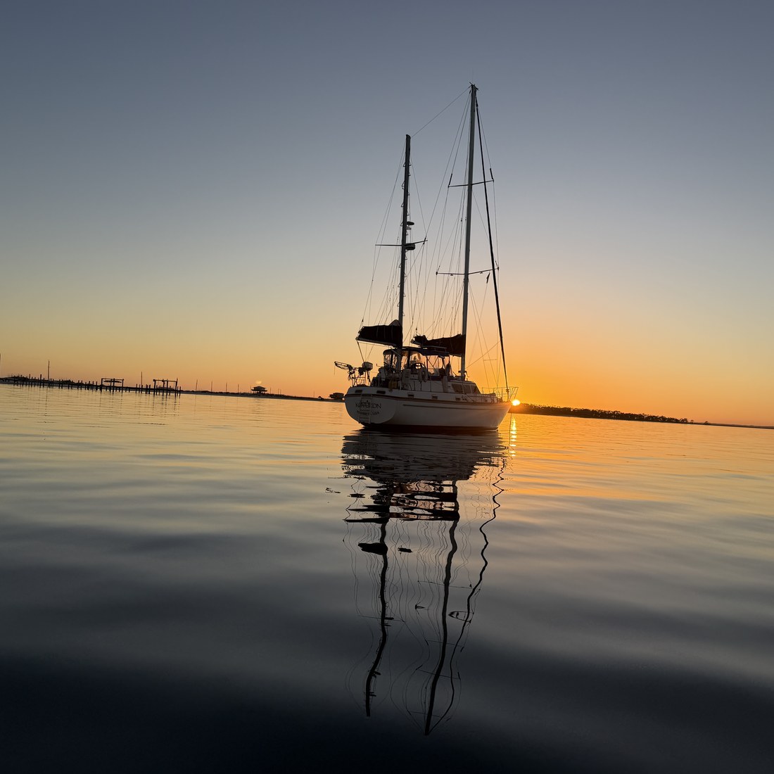 A sailboat silhouetted against the sunset on calm water